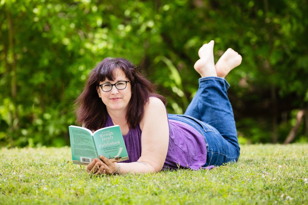 Kathryn Laying in a field reading her book, From Rough Draft to Published.